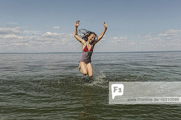Kleines Mädchen springt im Sommer am Strand ins Wasser