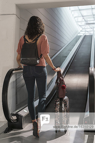 Junge Frau mit Koffer  die sich auf den Gehweg eines Flughafens bewegt