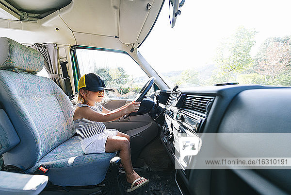 Girl wearing cap sitting on driver's seat in motor home