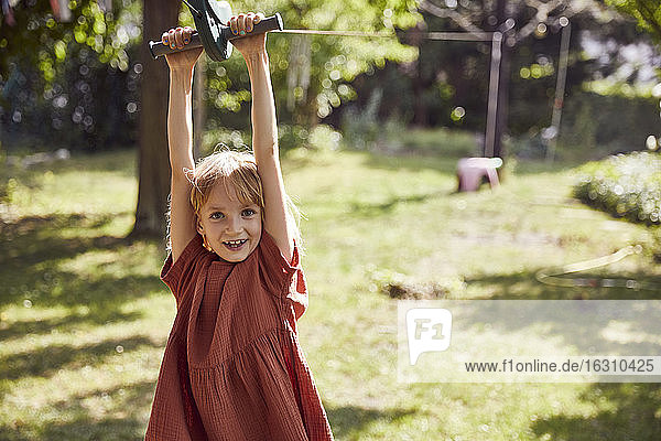 Fröhliches Mädchen hängt an einem Spielgerät im Hof