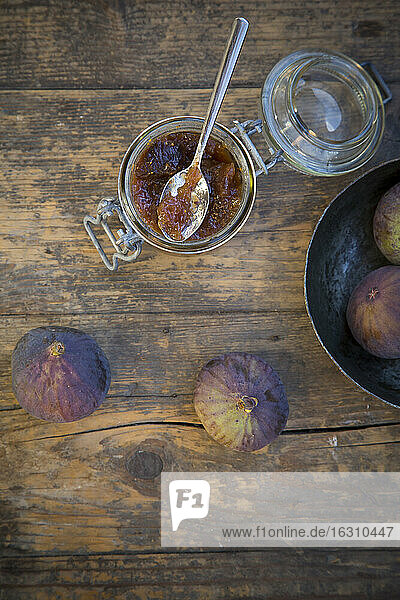 Vier Feigen (Ficus carica) und ein Glas mit Feigenmarmelade auf einem Holztisch  Studioaufnahme