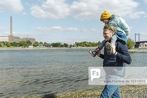Vater trägt Tochter auf der Schulter beim Spaziergang in der Nähe des Flussufers