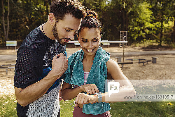 Sportlicher Mann und Frau schauen auf eine Smartwatch in einem Park