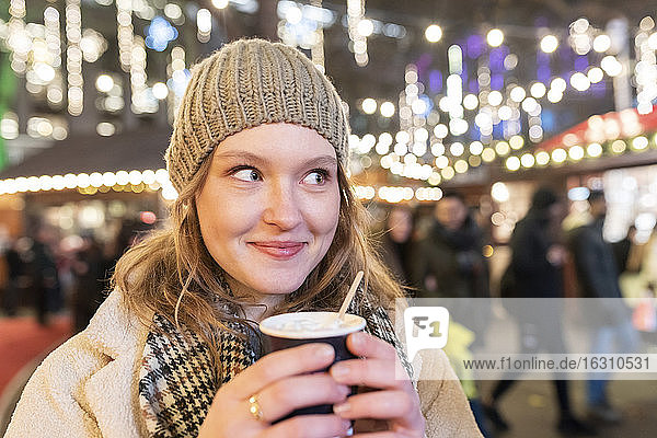 Nahaufnahme einer schönen Frau mit heißer Schokolade auf dem Weihnachtsmarkt bei Nacht