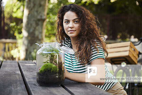Lächelnde Frau sitzt vor einem Glas mit Pflanzen