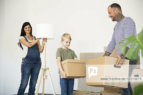 Frau steht mit elektrischer Lampe  während Vater und Sohn Kisten in ihr neues Haus tragen
