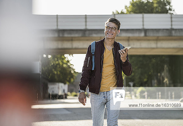 Lächelnder junger Mann  der beim Gehen auf der Straße ein Smartphone benutzt