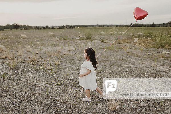 Cute girl with heart shape balloon walking in field