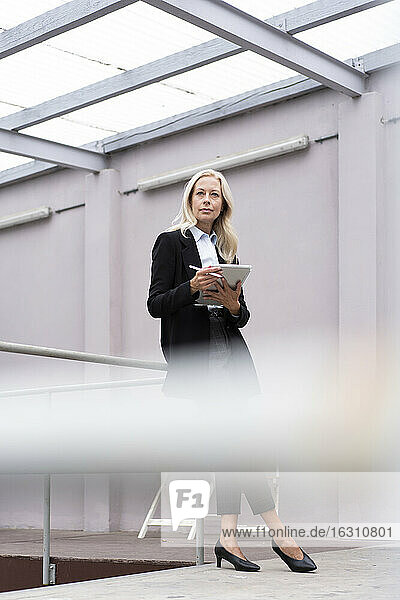 Geschäftsfrau mit digitalem Tablet an einem Geländer im Büro stehend