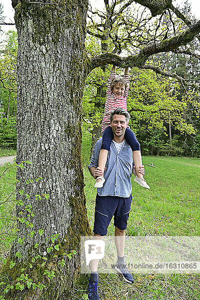 Lächelnder Vater trägt verspielte Tochter auf der Schulter im Wald