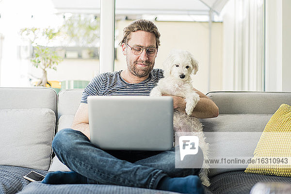 Mann mit Laptop und Hund auf dem Sofa sitzend
