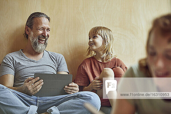 Cheerful father and daughter sitting against wall at home