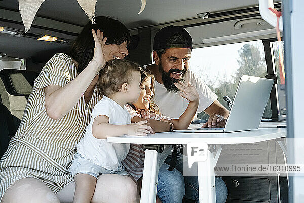 Fröhliche Familie winkt während eines Videogesprächs über einen Laptop in einem Van im Park