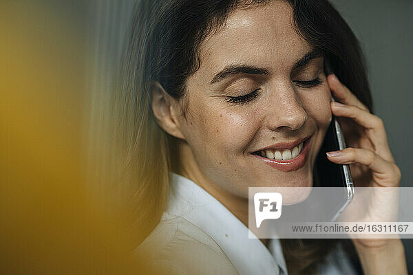 Junge Frau lächelt  während sie im Büro mit einem Mobiltelefon spricht