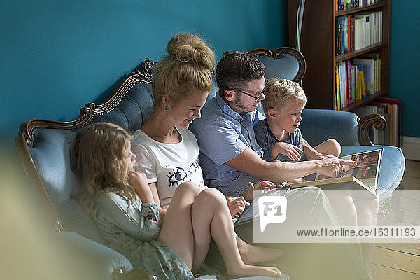 Familie schaut sich ein Fotoalbum an  während sie auf dem Sofa im Wohnzimmer sitzt