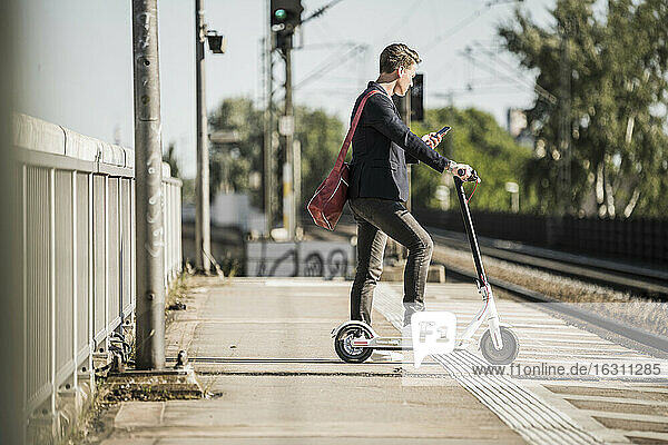 Mann  der sein Smartphone benutzt  während er mit seinem Roller am Bahnsteig wartet