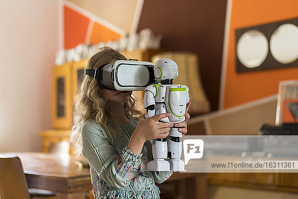 Mädchen mit Virtual-Reality-Simulator-Headset hält Roboter beim Spielen im Wohnzimmer zu Hause