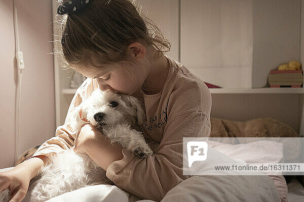 Nettes Mädchen umarmt Hund  während im Schlafzimmer sitzen