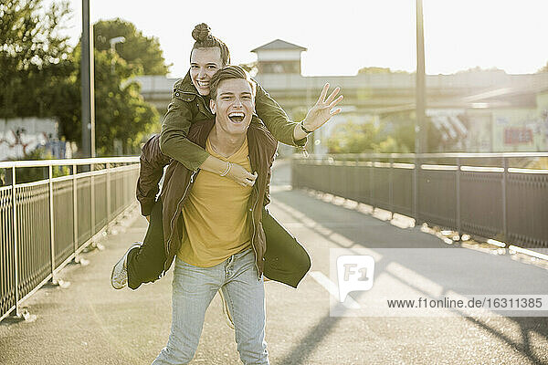 Fröhlicher junger Mann nimmt seine Freundin an einem sonnigen Tag in der Stadt Huckepack