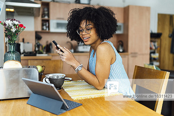 Unternehmerin mit lockigem Haar  die ihr Smartphone am Schreibtisch im Home Office benutzt
