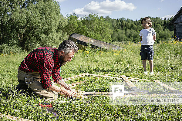 Junge betrachtet Zimmermann beim Bau eines Spielhauses an einem sonnigen Tag