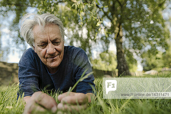 Confident smiling man looking at grass while lying in field