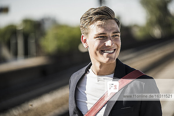 Lächelnder gut aussehender junger Mann  der am Bahnhof steht und wegschaut