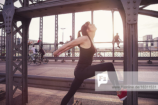 Woman exercising on bridge in city during sunset