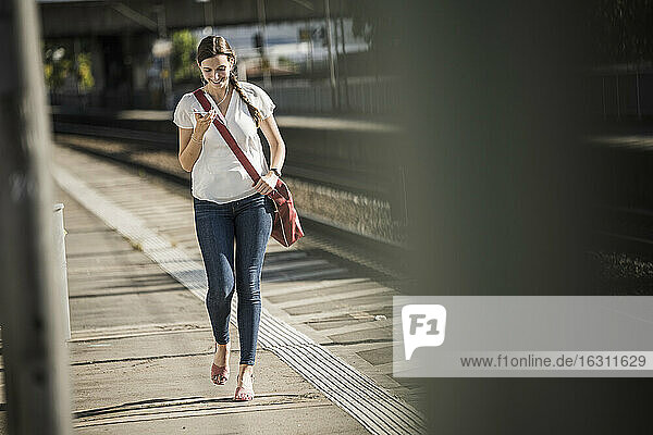 Young woman listening music through mobile phone while walking on railroad station platform