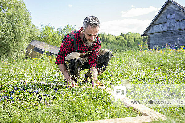 Carpenter crouching while positioning planks on grass