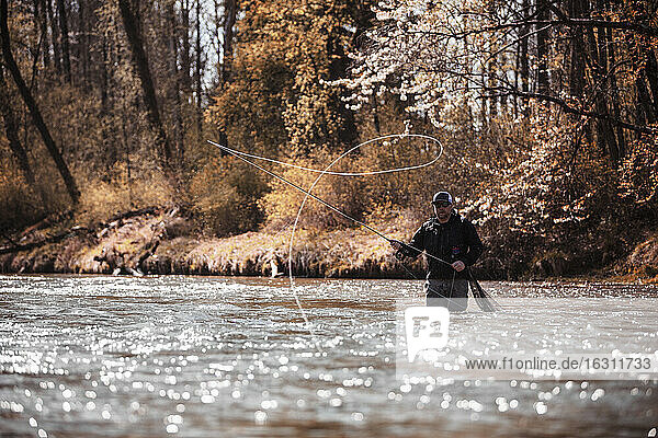 Fly Fisherman casting fishing line while standing in river at forest