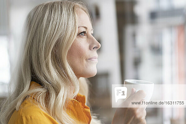 Nahaufnahme einer nachdenklichen Geschäftsfrau  die eine Kaffeetasse im Büro zu Hause hält  gesehen durch ein Fenster