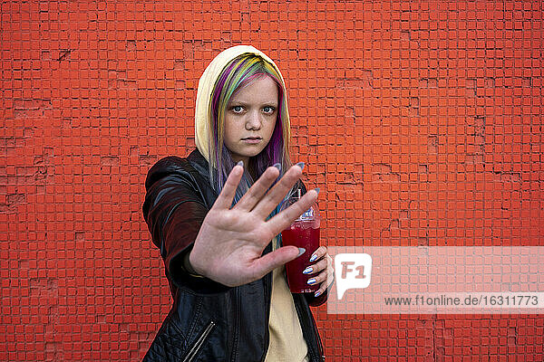 Porträt einer jungen Frau mit gefärbtem Haar  die ihre Hand vor einer roten Wand hebt