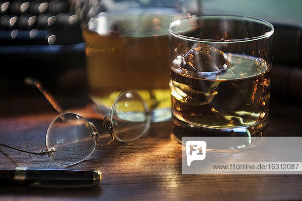 Whiskeyglas und Brille neben der Schreibmaschine auf dem Schreibtisch
