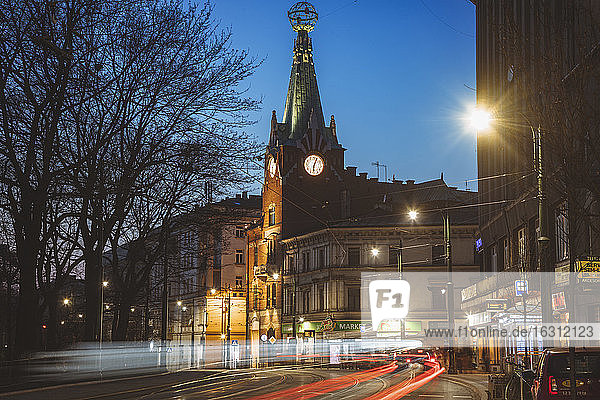 Polen  Kleinpolen  Krakau  Beleuchtete Stadtstraße mit Uhrturm bei Nacht