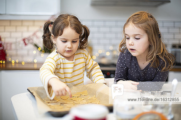 Two girls standing in kitchen  baking Christmas cookies.