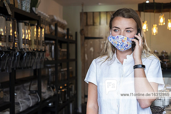 Frau mit Gesichtsmaske in abfallfreiem Geschäft vor Ort  mit einem Mobiltelefon