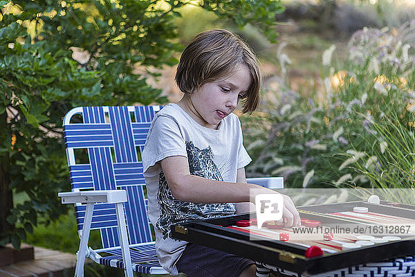 Ein kleiner Junge spielt Backgammon im Freien in einem Garten.