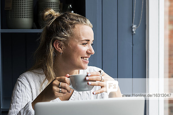 Junge blonde Frau  die allein an einem Cafétisch mit einem Laptop-Computer sitzt und aus der Ferne arbeitet.