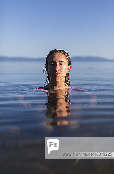 Teenager-Mädchen mit geschlossenen Augen  Kopf und Schultern in der Morgendämmerung über dem ruhigen Wasser eines Sees