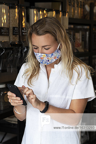 Woman wearing face mask shopping in waste-free local store  using a phone