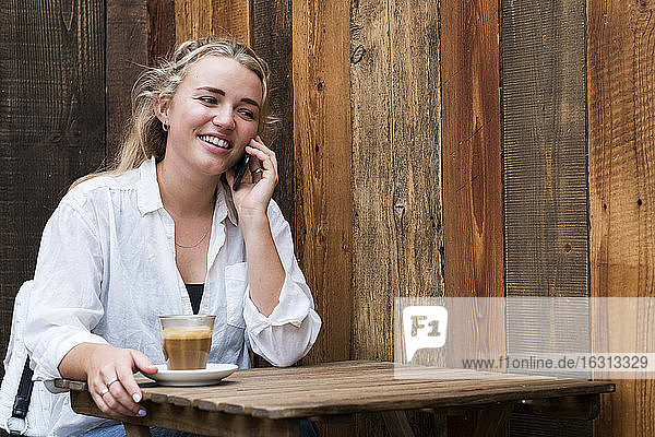 Junge blonde Frau  die allein in einem Café sitzt  ein Mobiltelefon benutzt und aus der Ferne arbeitet.