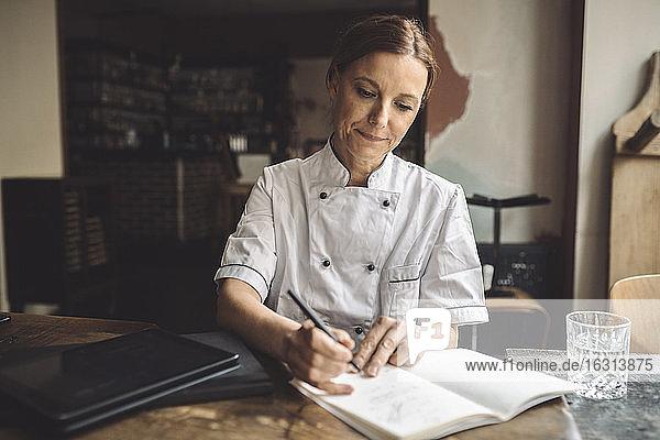 Mature chef writing in book at restaurant