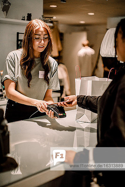 Female customer paying through smart phone to saleswoman at store