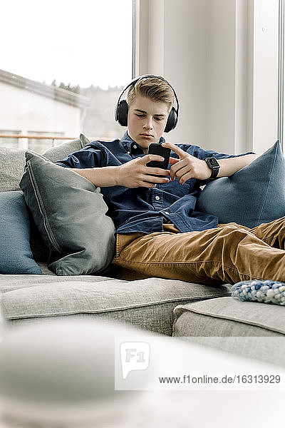 Teenager-Junge benutzt Smartphone  während er zu Hause Kopfhörer trägt