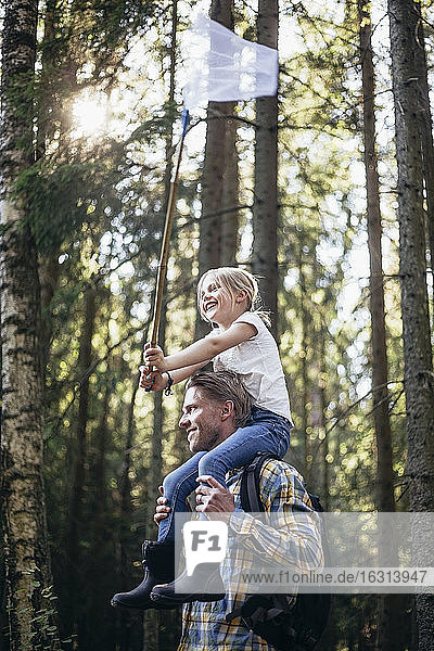 Tiefwinkelansicht eines lächelnden Vaters  der seine Tochter auf der Schulter mit einem Fischernetz im Wald trägt