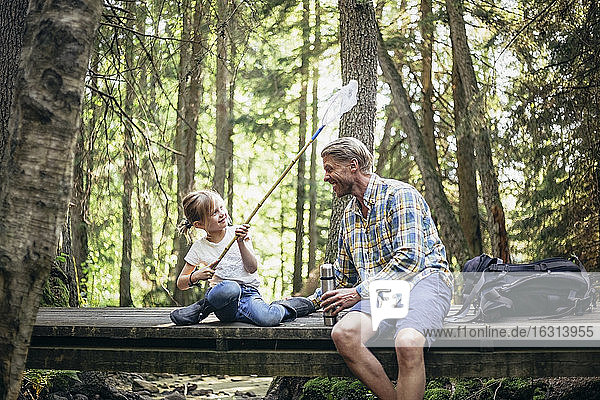 Lächelnde Tochter bespritzt Vater mit Wasser durch Fischernetz im Wald