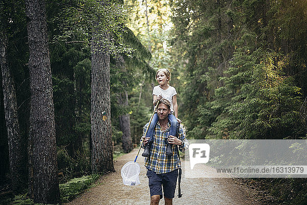 Vater trägt Tochter auf der Schulter beim Waldspaziergang