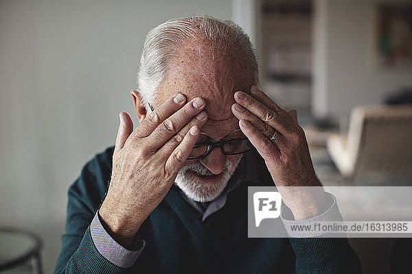 Besorgter älterer Mann mit dem Kopf in der Hand zu Hause