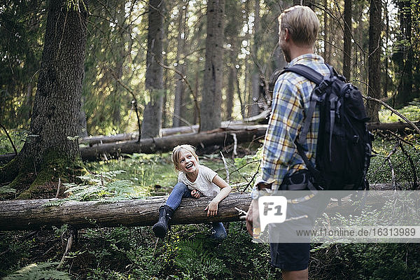 Lächelnde Tochter klettert über umgefallenen Baum  während sie den Vater im Wald anschaut